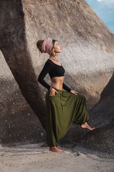 a woman standing in front of large rocks with her hands on her hips, wearing a black top and khaki pants