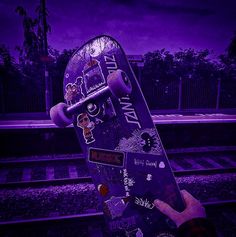 a person holding a skateboard in front of a train track with purple lighting behind them