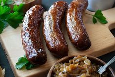 four sausages on a wooden cutting board next to bread and parsley sprigs