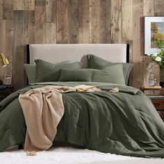 a bed with green sheets and pillows in front of a wooden paneled wall behind it