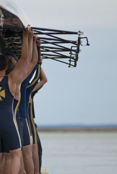 the men are carrying their boat over to the water's edge in preparation for competition