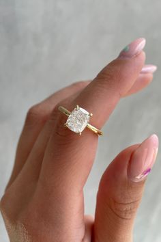 a woman's hand holding a ring with a square shaped diamond in the middle