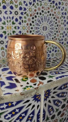 a gold cup sitting on top of a colorful tile wall with an ornate pattern behind it