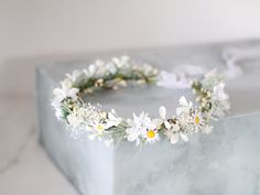 a white flower crown sitting on top of a marble block with greenery around it