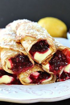 some crepes are stacked on top of each other with blueberry sauce and powdered sugar