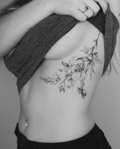 a woman's stomach with flowers and leaves tattooed on the side by her arm