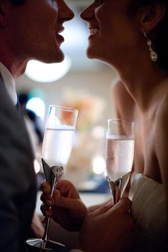 a man and woman holding wine glasses in their hands while looking into each other's eyes