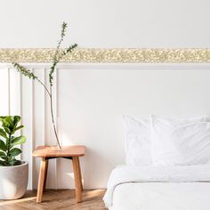 a bed with white sheets and pillows next to a potted plant on a wooden stool