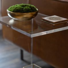 a glass table topped with a bowl filled with green moss sitting on top of it