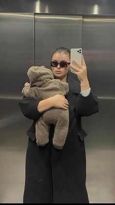 a woman taking a selfie in an elevator with a teddy bear on her arm