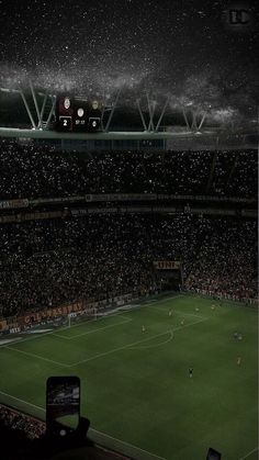 a soccer stadium filled with lots of people watching the game at night, while it is raining