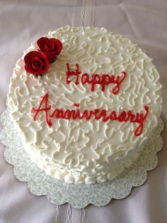 a white cake with red frosting and two roses on top that says happy anniversary