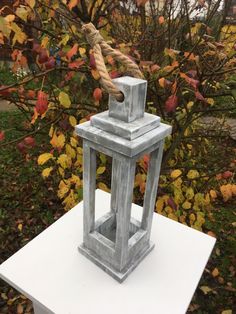 a white table topped with a small gray lantern and a rope hanging from it's top