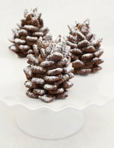 three small pine cones sitting on top of a white platter covered in powdered sugar