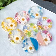 six glass dishes with flowers painted on them sitting on a white tablecloth next to green plants