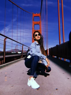 a woman sitting on the ground in front of a bridge with her legs crossed and wearing sunglasses