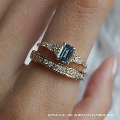 a woman's hand with three different rings on top of her finger and the ring has an emerald colored stone surrounded by white diamonds