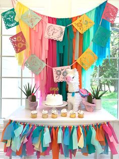 a cake and cupcakes on a table in front of a rainbow colored backdrop