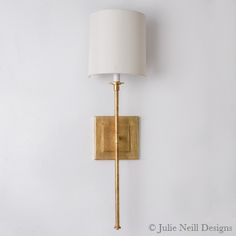 a gold wall light with a white shade on the side and a black lamp below it