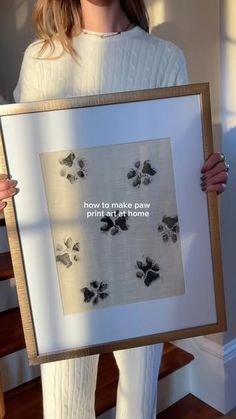 a woman holding up a framed art piece with words on it that reads, how to make paw prints at home