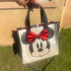 a hand holding a mickey mouse purse with a red bow on it's handle