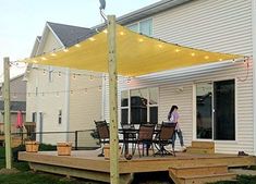 a woman walking across a deck under a yellow awning over a table and chairs