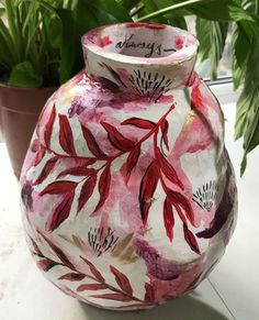 a painted vase sitting on top of a table next to a potted green plant