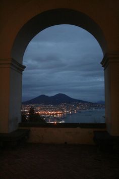 an arch with a view of the city lights and mountains in the distance at night