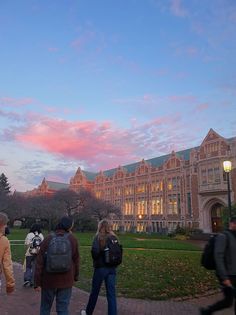 people walking in front of a large building at dusk with the sun setting behind them