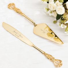 two gold - plated serving utensils are sitting on a table next to flowers