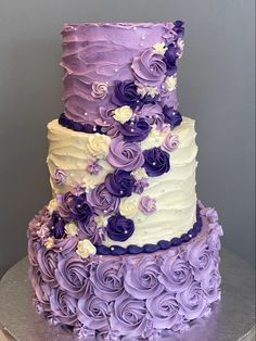 a three tiered cake with purple and white frosting flowers on it's side