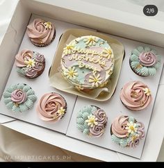 a birthday cake in a box surrounded by cupcakes with frosting and flowers