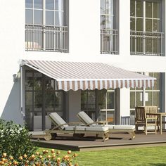 a large white building with an awning on the front and side of it, next to some lawn chairs