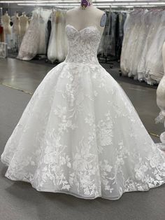 a white wedding dress is on display in a clothing store with other gowns and dresses behind it