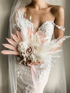 a woman in a wedding dress holding a bouquet with feathers and flowers on her shoulder