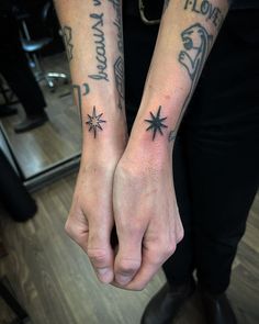 two people with tattoos on their arms holding hands and pointing at each other's fingers