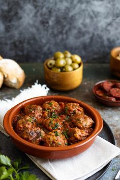 a bowl filled with meatballs next to bread and olives