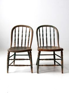 two wooden chairs sitting next to each other on a white surface with one chair facing the camera