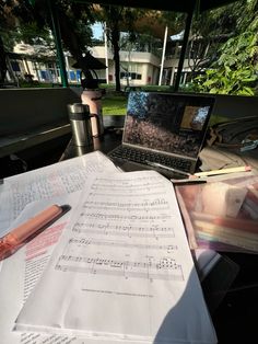 an open laptop computer sitting on top of a desk next to music sheets and a pen