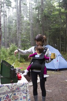 a woman holding a child in her back while camping