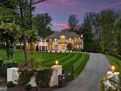 a large house with lots of windows and lights on it's front lawn at dusk