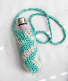 a crocheted water bottle cover on a white marble counter with a blue strap