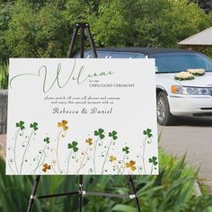 a welcome sign in front of a white car with flowers on it and greenery