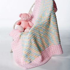 a pink teddy bear sitting in a crocheted blanket on top of a bed