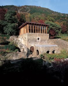 an old stone building sitting on top of a lush green hillside next to a forest