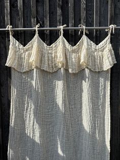 the curtains are hanging on the clothesline outside in front of an old wooden fence