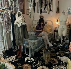 a woman sitting on top of a bed in a room filled with clothes and other items