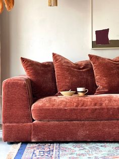 a red couch with two pillows on it in front of a painting and rugs