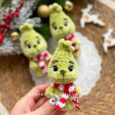 a hand holding a small stuffed animal in front of christmas decorations and ornaments on a table