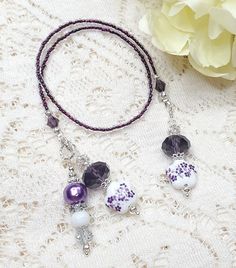 two necklaces with purple and white beads on a lace tablecloth next to flowers